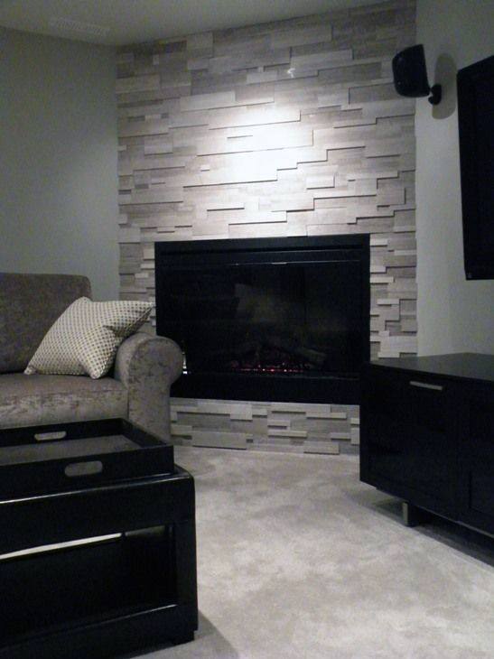 Modern living room with gray stacked-stone corner fireplace, gray sofa, and black storage furniture.