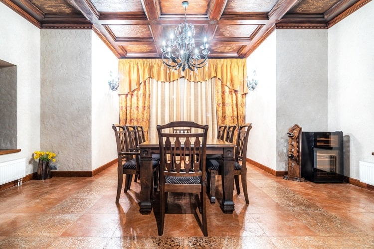 Elegant dining room with a wooden table, chairs, chandelier, and golden curtains beneath a coffered ceiling