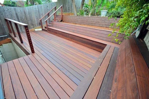Wooden deck with built-in bench seating, surrounded by greenery and a wooden fence