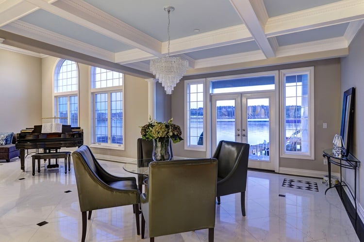 A luxurious dining area with a coffered ceiling, elegant chandelier, large windows offering scenic views, and sophisticated furniture, creating a serene and stylish atmosphere