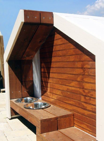 Wooden dog house with two metal bowls on a platform outside