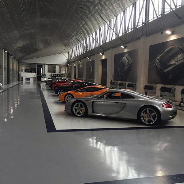 A sleek, spacious garage showcasing luxury sports cars under a high arched ceiling, with large automotive artwork on the walls.