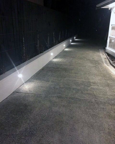 Driveway illuminated with recessed lighting along a clean, white wall, creating a sophisticated and inviting look at night
