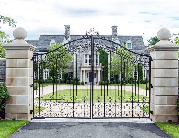 Grand wrought iron driveway gate with intricate scrollwork and arched top design.