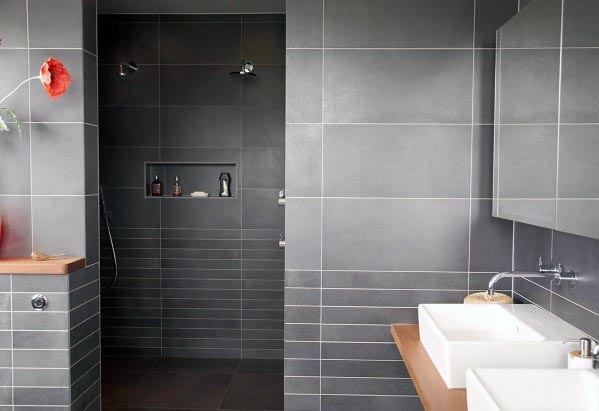 A sleek gray-tiled bathroom featuring a walk-in shower and a double vanity with wooden accents.