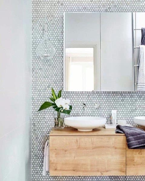 A stylish bathroom with a wood vanity, white vessel sink, hexagonal tile wall, and sleek mirrored cabinet.