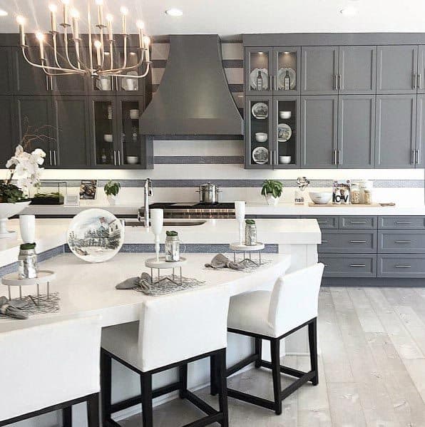 Luxury grey kitchen with glass cabinets, white countertops, and a statement chandelier.