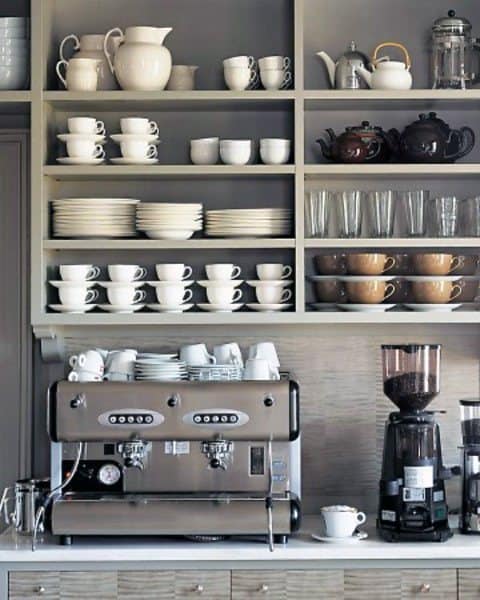 Coffee bar with open shelves, espresso machine, coffee grinder, cups, teapots, and glassware.