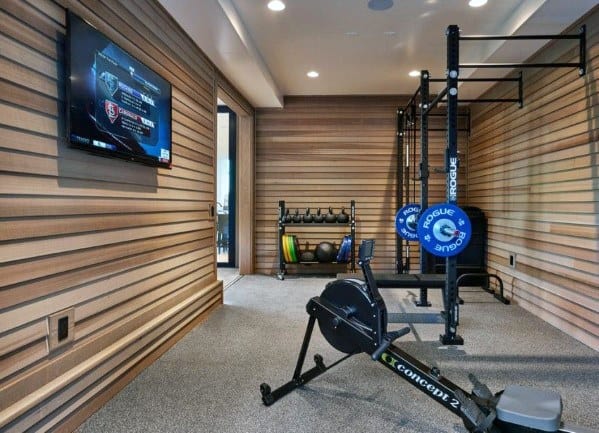 Home gym with wooden panel walls, rowing machine, pull-up bar, and wall-mounted TV.