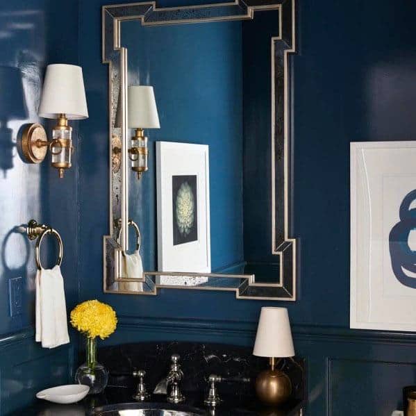Luxury bathroom with navy walls, ornate mirror, wall sconces, and marble countertop.