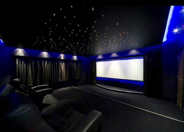 A home theater with black recliners, a large screen, starry ceiling lights, and blue accent lighting