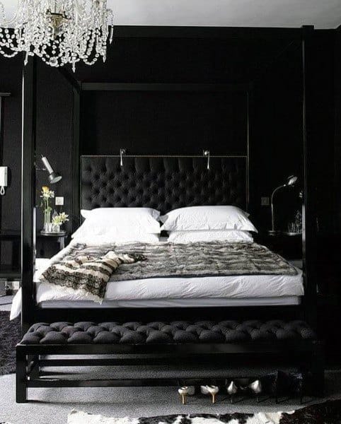 Elegant black bedroom with a four-poster bed, tufted headboard, chandelier, and luxurious bedding.