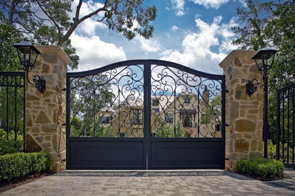 Ornate black iron driveway gate with swirling scrollwork and arched top design.