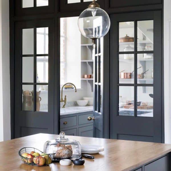 Glass-paneled black pantry doors with a view of a stylish kitchen interior.