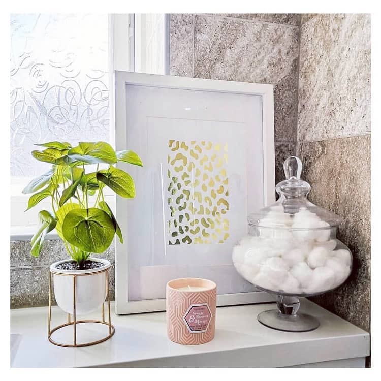 Bathroom shelf with plant, framed art, pink candle, and jar of cotton balls.
