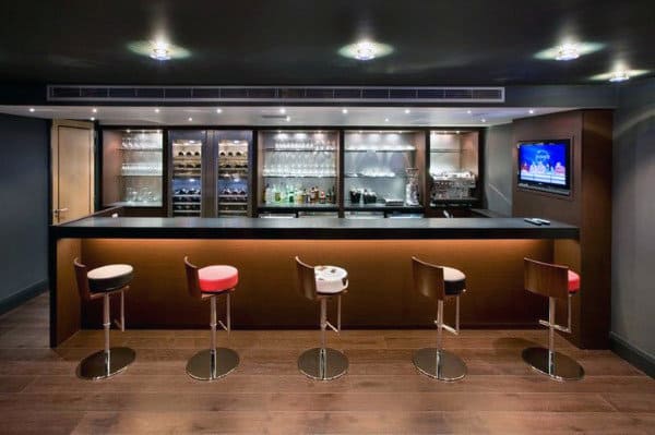 Modern bar with four stools, backlit shelving stocked with glasses and bottles, and a wall-mounted TV