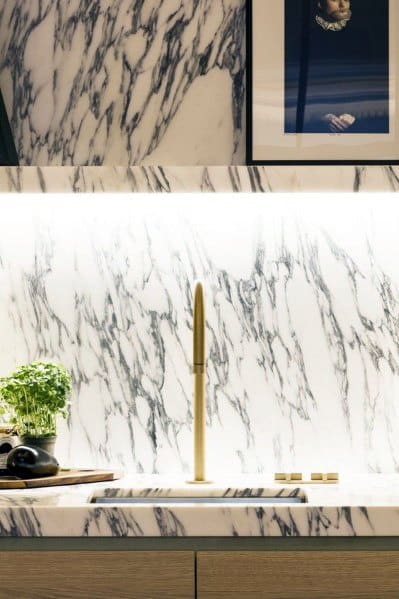 Luxury kitchen with dramatic white marble backsplash, warm under-cabinet lighting, and a sleek gold faucet
