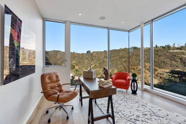 Modern home office with glass walls, scenic mountain view, and stylish leather chairs.
