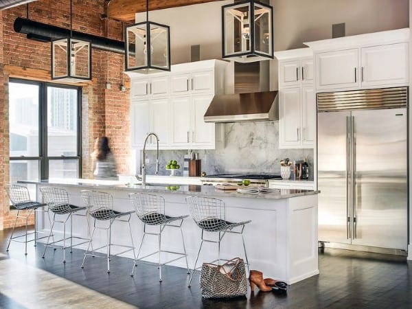 Industrial-style kitchen with white cabinets, exposed brick walls, and metal barstools.