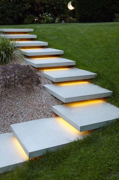 Floating concrete steps with integrated LED lighting surrounded by grass and gravel.