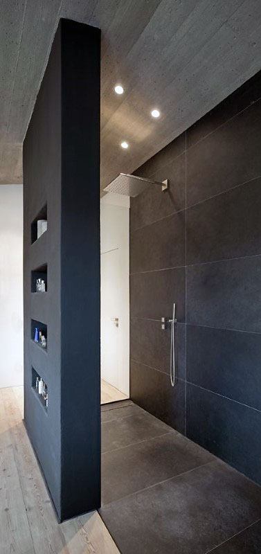 Sleek shower with dark matte tiles, recessed storage shelves, and minimalist fixtures.