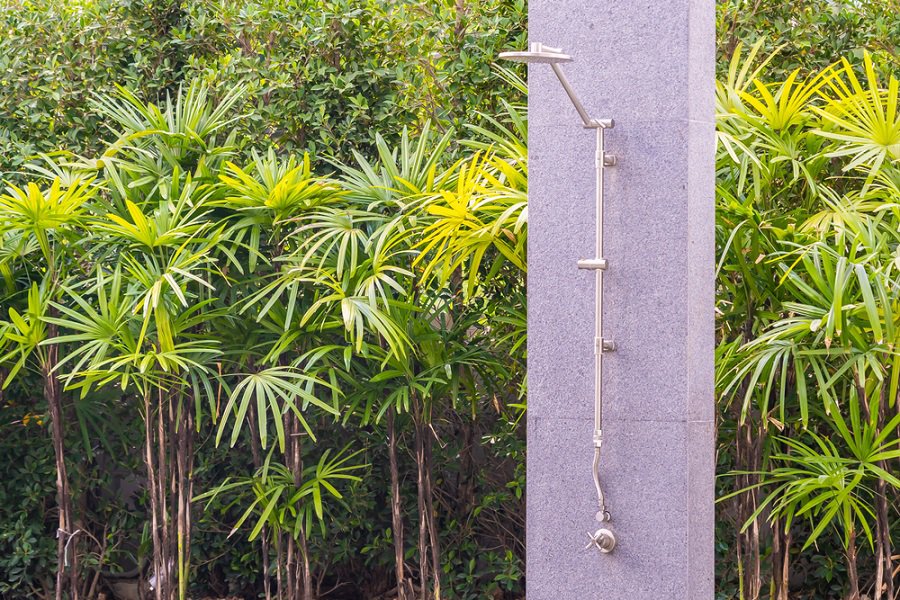 Modern outdoor shower with sleek stainless steel fittings, set against lush green foliage.