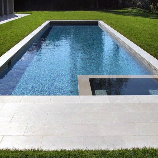 Modern rectangular pool with sleek mosaic tiles, grassy borders, and a stone pool deck.