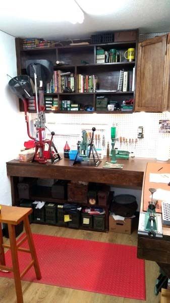 Functional reloading bench with mounted presses, wooden cabinets, organized pegboard tools, and ample storage space below