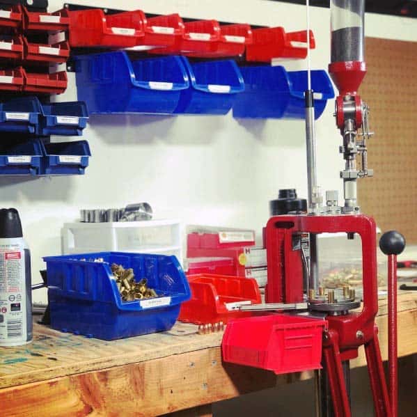 Reloading bench with a red press, labeled blue and red bins for components, and a sturdy wooden work surface