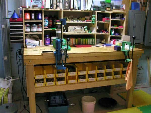 Organized reloading bench with mounted presses, labeled yellow bins, and wooden shelves stocked with tools and supplies