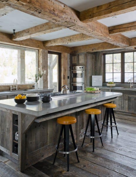 Rustic kitchen with reclaimed wood beams, gray island, yellow stools, and large windows.