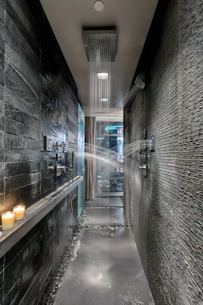 Modern shower with sleek fixtures, dark stone walls, and candles on the floor shelf