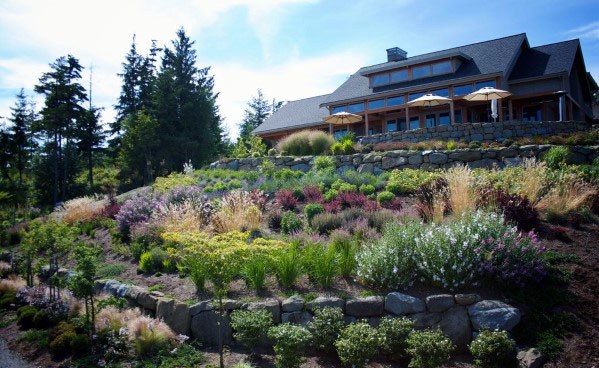 Luxury sloped backyard with colorful plants, stone retaining walls, lush greenery, and a beautiful house with a scenic view