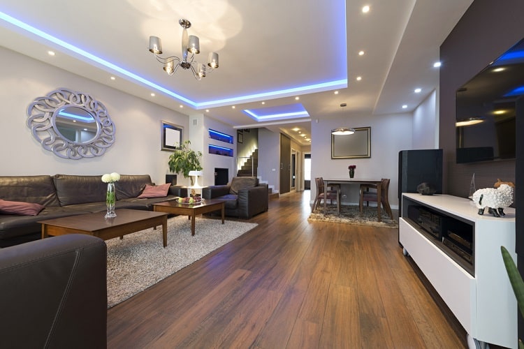 The ceiling features a modern design with recessed spotlights and vibrant blue cove lighting, adding a luxurious touch to the spacious living room