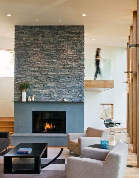 Modern living room with a dark stacked stone fireplace, sleek furnishings, and an open mezzanine view
