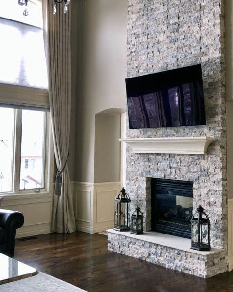 Elegant stacked stone fireplace with a white mantel, mounted TV, and decorative lantern accents