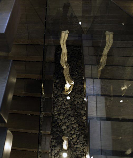 Aerial view of a modern staircase with glass railing, featuring pebbles and driftwood decor beneath