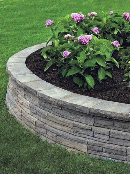 A circular stone retaining wall surrounding vibrant hydrangea flowers, enhancing the garden with a neat, structured border