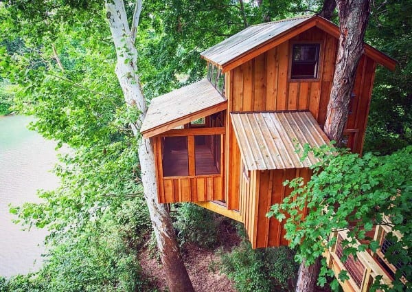 Wooden treehouse nestled among green trees with a view of a river in the background