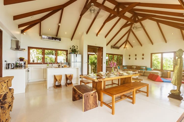 Spacious open-plan room with wooden beams and high ceilings, dining table, kitchen, and seating area filled with natural light