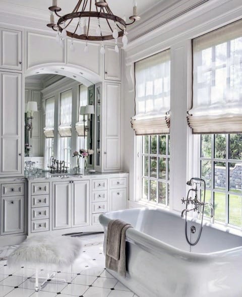 Luxurious white bathroom with crown molding, freestanding tub, natural light, marble counters, and gold accents
