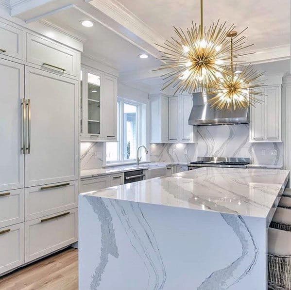 White kitchen with marble waterfall island, gold starburst pendant lights, and modern cabinetry.