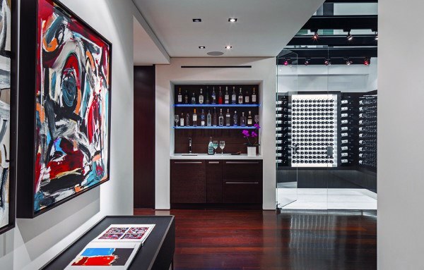 Modern room with abstract art, a wine bar with bottles, and a wine cellar displaying vintages behind a glass door