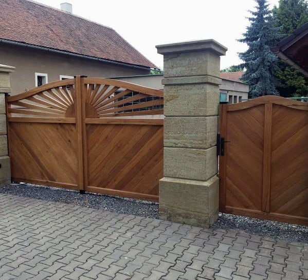 Wooden gate with sunburst pattern and stone pillars on a paved driveway