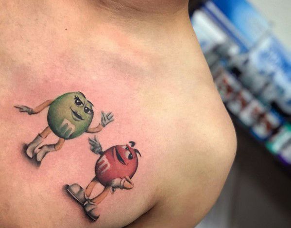Tattoo of animated M&M’s characters, featuring the green and red candies with expressive faces and playful poses in a detailed design.