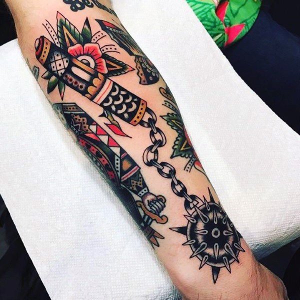 Bold traditional-style mace tattoo featuring a spiked ball on a chain, a decorated handle, and vibrant floral elements, symbolizing power and resilience.