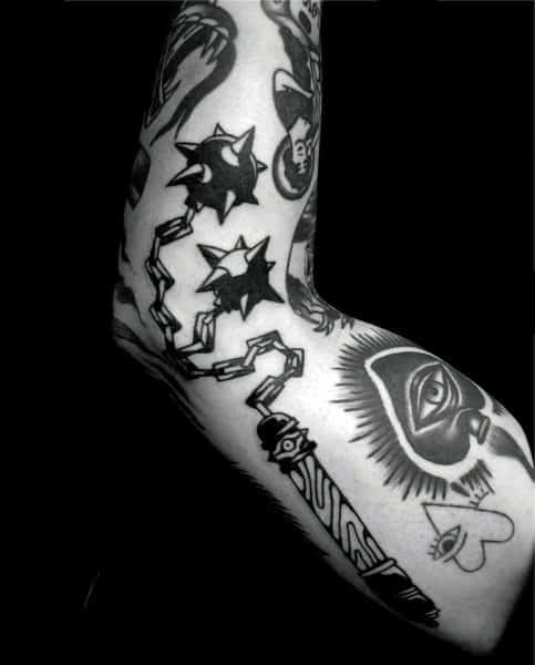Bold black ink mace tattoo featuring dual spiked balls on a chain, connected to a decorated handle, symbolizing strength, battle, and resilience.