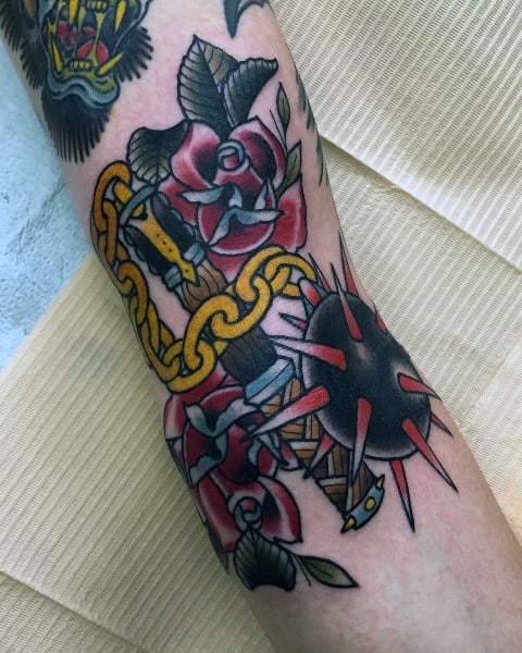 Colorful mace tattoo featuring a spiked ball, golden chain, dagger, and vibrant red roses, symbolizing strength, passion, and resilience.