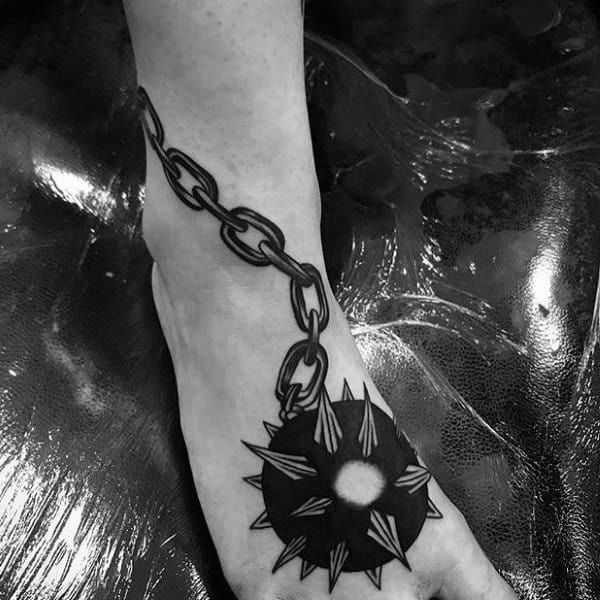 Black ink mace tattoo featuring a spiked ball on a heavy chain wrapping around the ankle, symbolizing strength, resilience, and power.