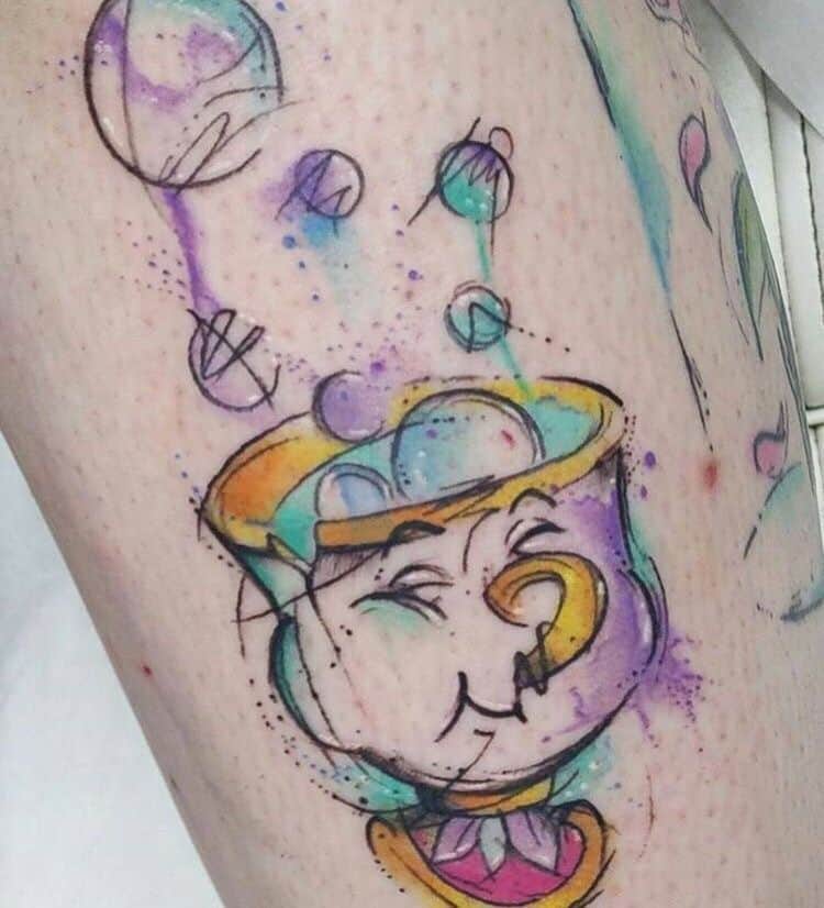 Watercolor-style tattoo of Chip from Beauty and the Beast, featuring playful bubbles and splashes of purple, blue, and yellow ink.